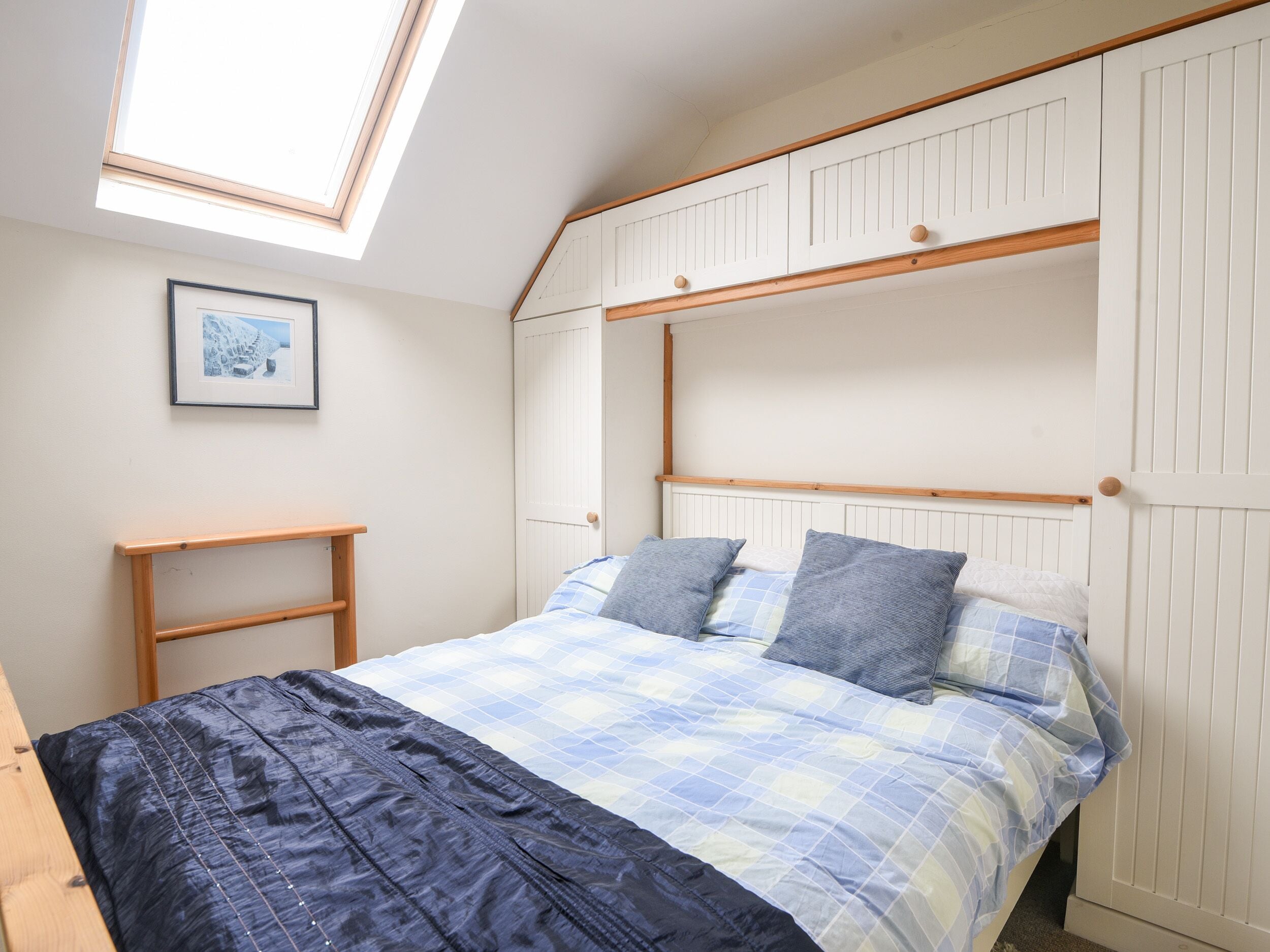Une chambre avec un lit superposé, une lucarne, une table de chevet et un tableau encadré au mur.
