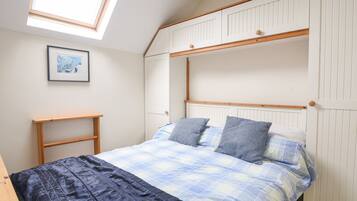 Une chambre avec un lit superposé, une lucarne, une table de chevet et un tableau encadré au mur.