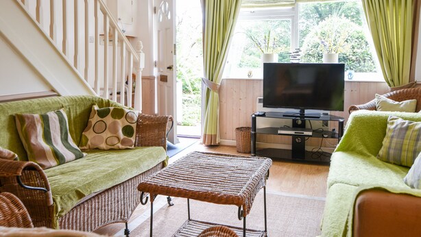 Una sala de estar con un sofá, una mesa de mimbre, un televisor y una ventana con cortinas.