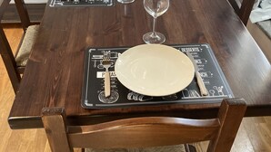 A wooden dining table with placemats, plates, and wine glasses set for a meal.