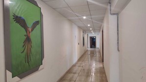 Een lange, smalle gang met een betegelde vloer en een groot ingelijst schilderij van een vogel aan de linkerwand.