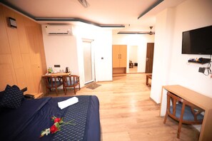 A hotel room with a bed, a desk, a chair, a TV, and a kitchenette. - Hotel Noida Grand (Noida)