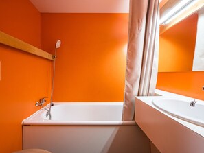 A bathroom with an orange wall, a white bathtub, and a white sink. - Bright renovated studio · Sleeps 4 · South/west balcony (Les Arcs 1800)