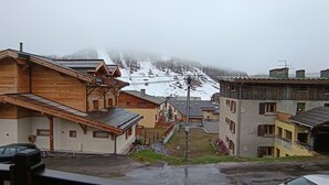 A mountain village with wooden buildings, a ski lift in the background, and a snowy landscape.