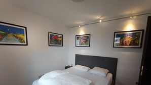 A neatly made bed with white linens in a room with three framed artworks on the walls.
