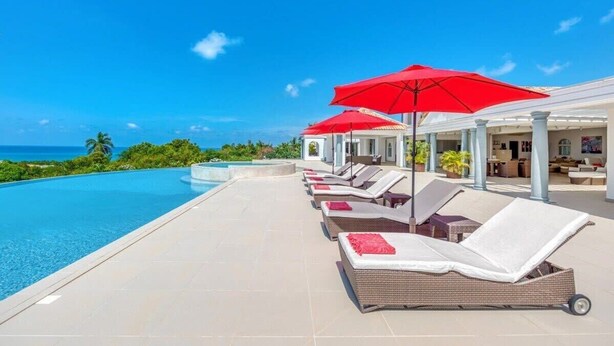 Ein Poolbereich mit Liegestühlen und roten Sonnenschirmen, mit Blick auf einen klaren, blauen Himmel und das Meer.