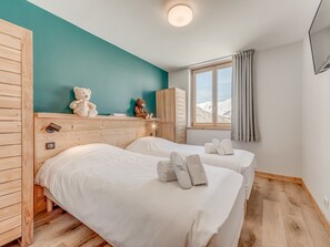 A room with two beds, a wooden wardrobe, a window with a view of mountains, and a teal wall. - Renovated Apartment in Tignes - 8 Pax, 82m², Wifi Included (Tignes)
