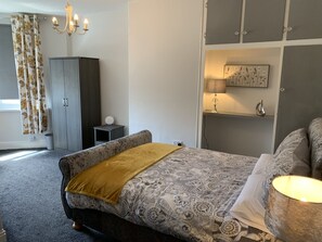 Une chambre à coucher comprenant un lit, une armoire, une table de chevet, une lampe et une étagère murale ornée d’un tableau.