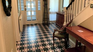 A hallway with a checkered floor, a wooden chair, a wooden table, and a staircase with a white railing.