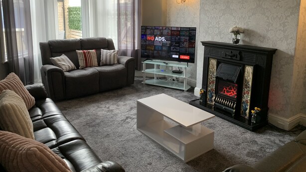 A living room with a dark leather sofa, a white coffee table, a fireplace, and a TV on a stand.