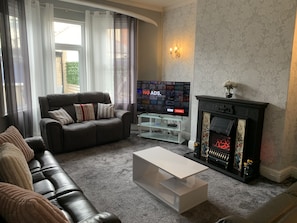 A living room with a dark leather sofa, a white coffee table, a fireplace, and a TV on a stand. - Heather Glen 6 Bedroom 6 Bathroom Home by the sea (Blackpool)