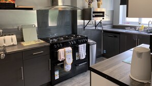 A modern kitchen with a stainless steel range hood, a built-in oven, a dishwasher, and a window above the sink.