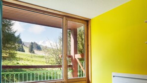 A room with a wooden bench, a small round table, and a view of a green landscape through a large window.
