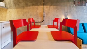 A dining area with red chairs and a white table, a hanging light fixture, and a blue couch in the background.