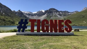 Un cartello con l'hashtag #TIGNES sullo sfondo di un paesaggio montuoso con un lago.