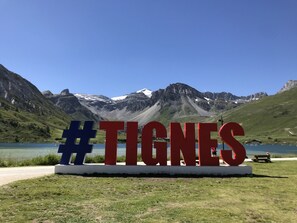 A sign with the hashtag #TIGNES in front of a scenic mountain lake.
