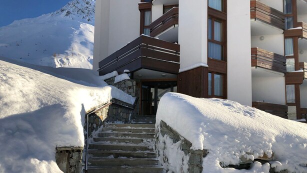 Una scala coperta di neve che conduce a un edificio con facciata in pietra e balconi in legno.