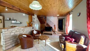 Un salon chaleureux avec une cheminée en pierre, des canapés en cuir, un plafond en bois et un téléviseur.