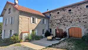 Ein zweigeschossiges Steinhaus mit rotem Ziegeldach, einer Veranda mit Tisch und Stühlen sowie einer Holztür.