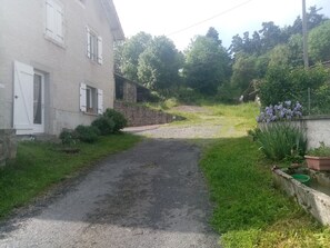 Un chemin de gravier mène à une maison avec un mur en pierre et un jardin fleuri.