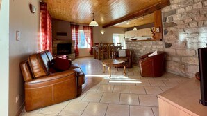 Un salon chaleureux avec une cheminée en pierre, un canapé en cuir et un coin repas avec des chaises en bois.