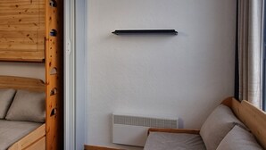 A compact room with a wooden bunk bed, a white wall, a black shelf, and a white air conditioning unit.