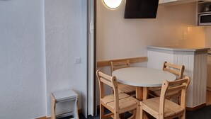 A compact kitchen with a round table and wooden chairs, a built-in TV, and a small side table.