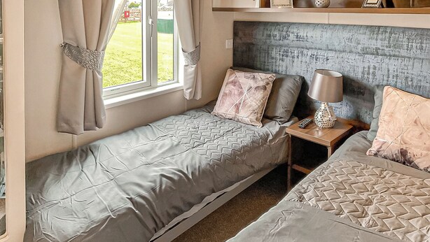 Una habitación compacta con dos camas, una mesita de noche con lámpara y una ventana con cortinas.