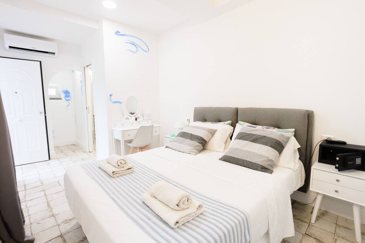 A hotel room with a bed, bedside table, desk, and a mirror.