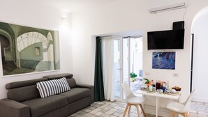 A living room with a grey sofa, a dining table with chairs, a flat-screen TV, and artwork on the walls. - Suite Saint Michael (Capri)
