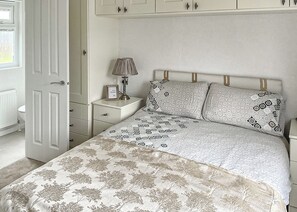 A bedroom with a bed, nightstand, lamp, and a door.