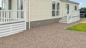 Une maison mobile de plain-pied avec un porche à l’avant, une petite terrasse et une allée gravillonnée.