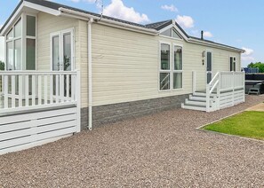 A single-story mobile home with a front porch, a small deck, and a gravel driveway.