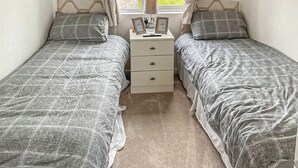Une chambre avec deux lits simples, une table de chevet avec une lampe et une fenêtre avec des rideaux.