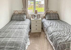 Une chambre avec deux lits simples, une table de chevet avec une lampe et une fenêtre avec des rideaux.