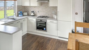 Una cocina moderna con armarios blancos, una estufa a gas, un horno y una ventana con vistas a un jardín.