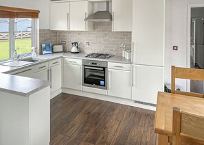 Une cuisine moderne avec des meubles blancs, une cuisinière à gaz, un four et une fenêtre donnant sur un jardin.
