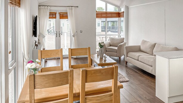 Una sala de estar moderna con una mesa de comedor de madera, dos sofás y un ventanal con cortinas.
