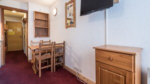 A room with a wooden desk, a television mounted on the wall, a mirror, and a door leading to another room.