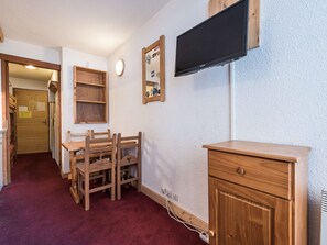 Quarto com escrivaninha de madeira, televisão fixada na parede, espelho e porta que dá para outro espaço.
