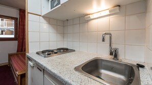 A kitchen with white tiles, a stainless steel sink, a stove, and a window with a view of a balcony.