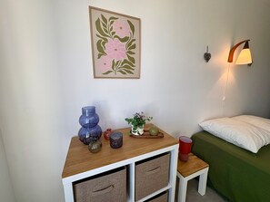 Una stanza con un letto, un piccolo tavolo con oggetti decorativi, una lampada a parete e un quadro floreale incorniciato.
