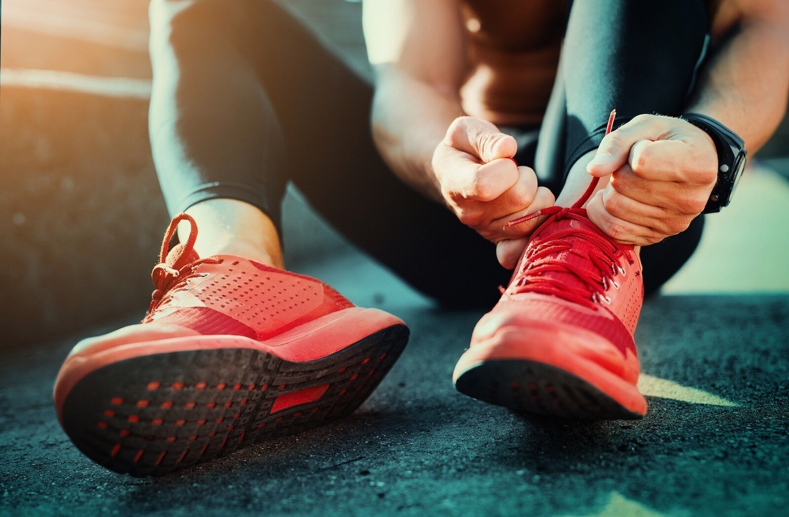 Une personne est en train d’attacher les lacets de ses chaussures de course rouges.