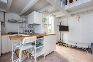A kitchen with a wooden countertop, white cabinets, a white chair, a TV on a stand, and a window. - GuestHost - NEW! Apt at 700mt from Corso Lodi! x3 (Milan)