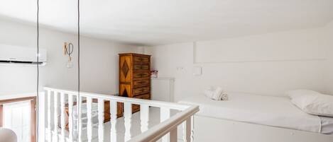 A white room with a bed, a wooden dresser, and a white railing.