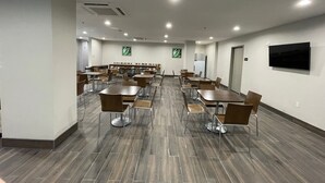 A conference room with multiple tables and chairs, a flat-screen TV mounted on the wall, and a refrigerator in the background. - Days Inn by Wyndham Bronx NYC (Bronx)