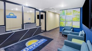 A reception area with a Days Inn sign, a reception desk, a seating area with blue chairs, and a large window with a view of greenery. - Days Inn by Wyndham Bronx NYC (Bronx)