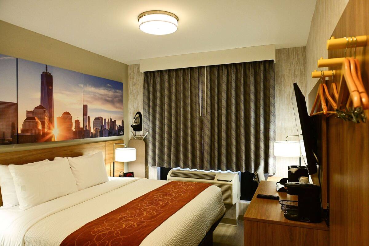 Een hotelkamer met een groot bed, een stadslandschap schilderij, een bureau met een lamp en een televisie.