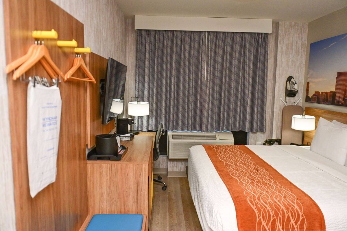 Een hotelkamer met een bed, bureau, stoel en uitzicht op een stadsbeeld.