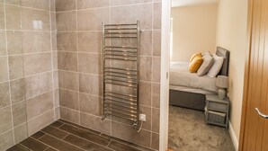 A bathroom with a towel rack, a shower, and a bed visible through an open door. - Trewen (Pwllheli)